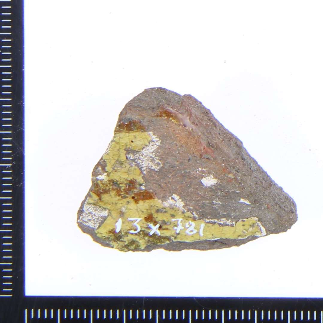 Et lille fragment med rester af gul/rødlig glasur.