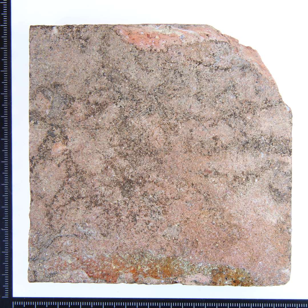 Et kvadratisk rødbrændt gulvflise lettere fragmenteret. Med rester af rødlig glasur. Mål:11x11x2 cm.