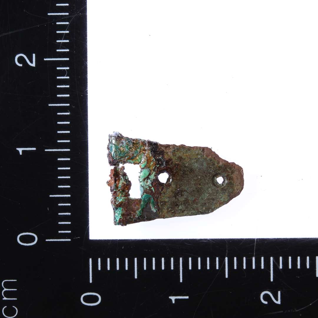 Lille 1,5 x 1 cm del af spænde i bronze. Muligvis del af bogspænde.

Bolt-Jørgensen 2019: Malle