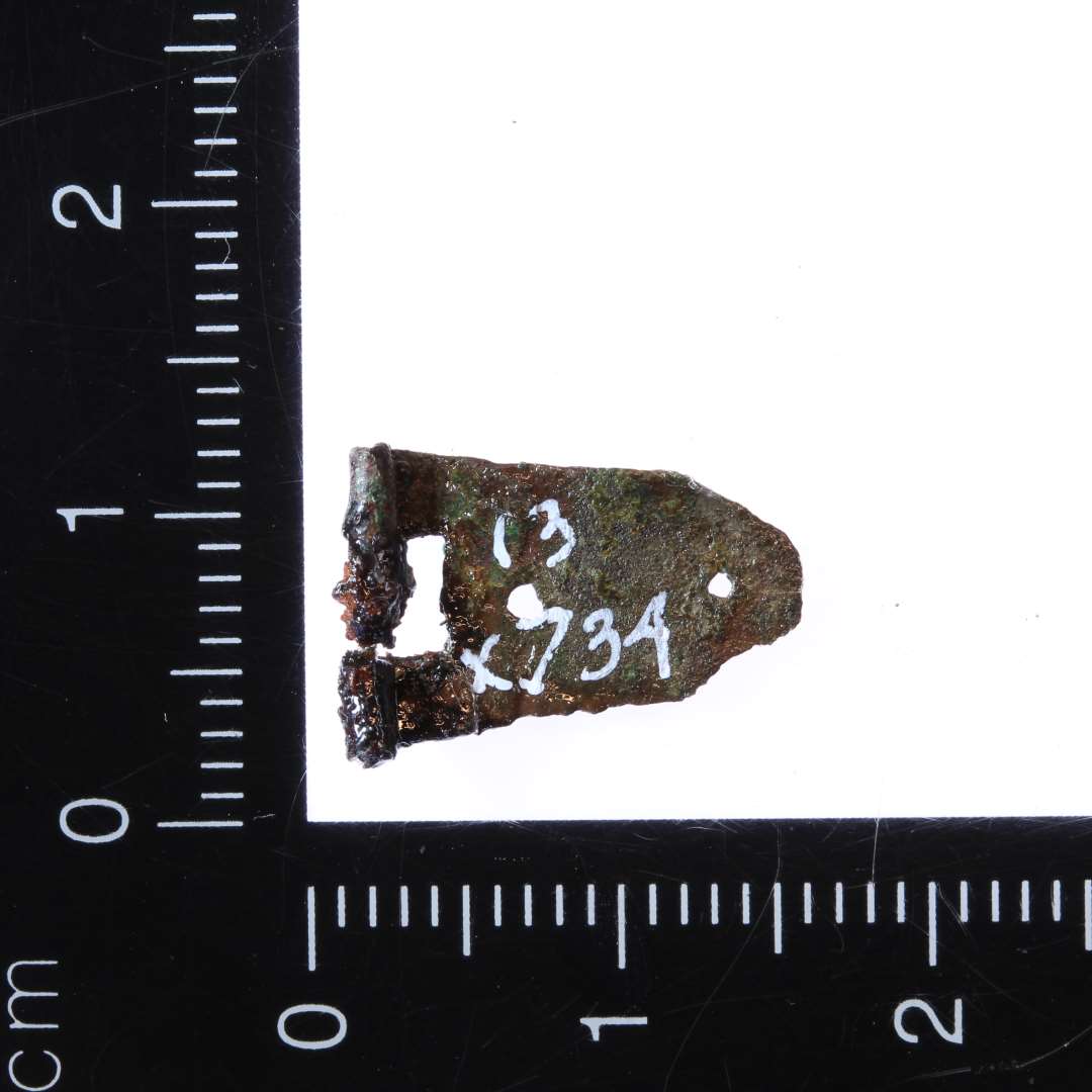 Lille 1,5 x 1 cm del af spænde i bronze. Muligvis del af bogspænde.

Bolt-Jørgensen 2019: Malle