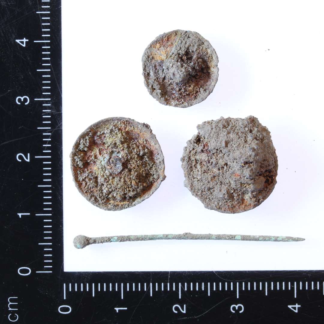 Tre knapper af kobberlegering, samt en bronzenål. Knapperne er konvekse. En mindre med ca. dia. på 1 cm og to størrer med ca. dia på 1,5 cm. Nålen mpler 4 cm.
