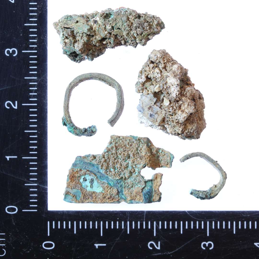 Div fragmenter af kobberlegering. To stykker afklippet tynd tråd bøjet som ringe. En korroderet klump og et fragment af en tynd plade med nittehul.