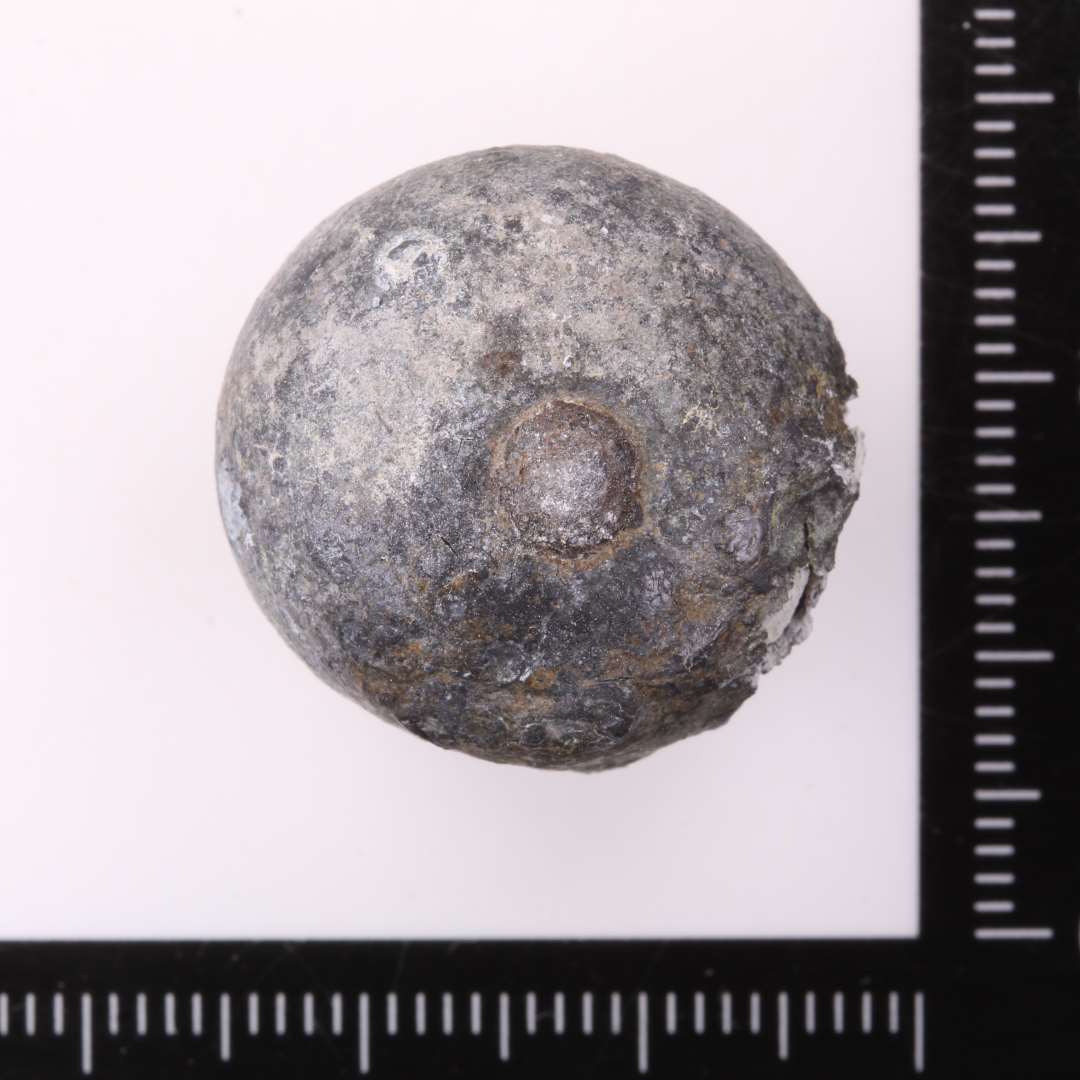 Kugleformet, Ø ca. 1,8-2,2 cm. Lille 'dut' af antagelig jern, stikker frem på den ene side.