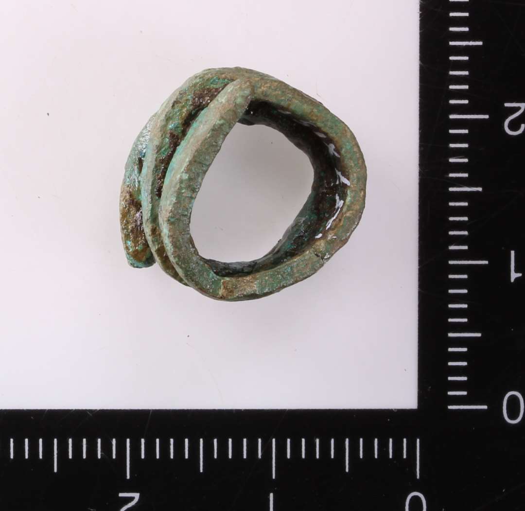 Mindre bronzestykke oprullet i spiral (med smletning for øje?). Diam. c. 1,5 cm, selve bronzen ca. 3x2 mm.