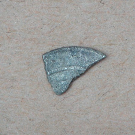 Ganske lille fragment af formodet kufisk mønt, ca. 8 x 5 mm. Kun ganske lidt synlig tekst på den ene side. Præget i AH284 = 897 e.Kr (Jf. K41). dirhem