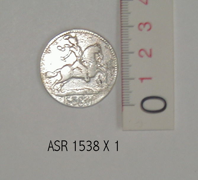 En sølvmønt, der er et afslag af en guldmønt, præget i Chr. D V`s tid. På møntens forside ses en rytter med en depeche i hånden. På bagside er  tre Cèr flettet ind i hinanden og i åbningerne i det herved opståede mønster er indflettet romertallet V. Kanten er på begge side riflet.  Mål: møntens diameter 3 cm.         møntens tykkelse 1 mm.  Vægt: 11,46 g.