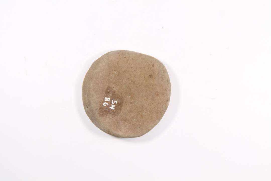 1 stk. flad, cirkulær, brunlig sten. Diameter: ca 5,5 cm.