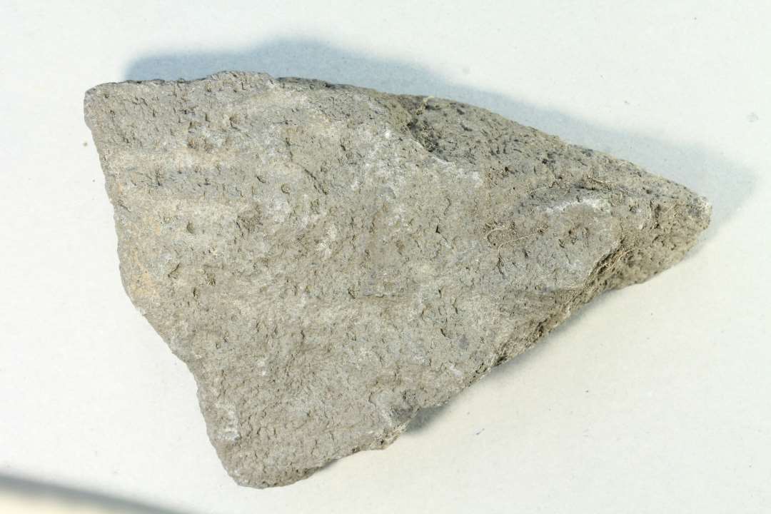 Randfragment, ca. 11x7x3 cm Slidflade bevaret, den anden side ret groft og ujævnt behuget, derfor nok ÆMIA.