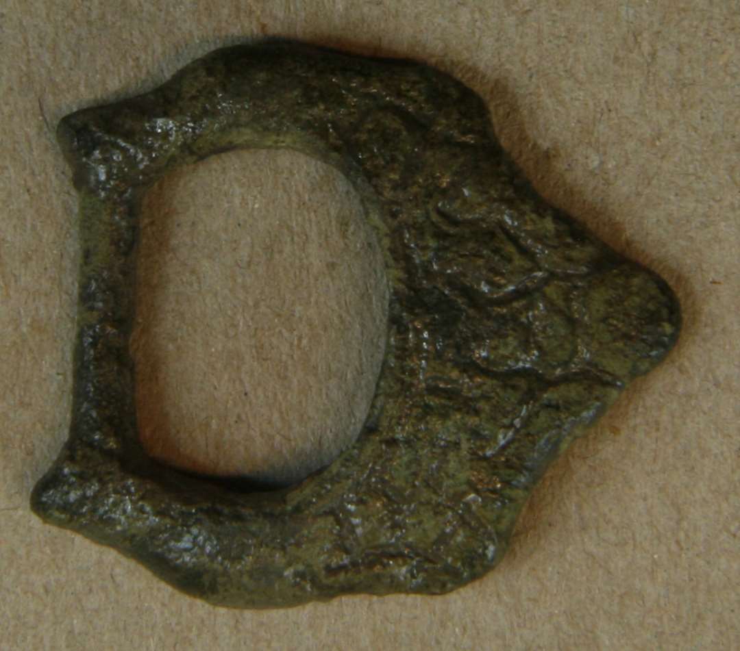 Bøjlen af et vikingetids remspænde med fast bagaksel. Den forreste del af bøjlen er bred, tilspidset og ornamenteret med fletbånds- eller dyreornamentik. Højde: 25 mm., bredde: 28 mm.