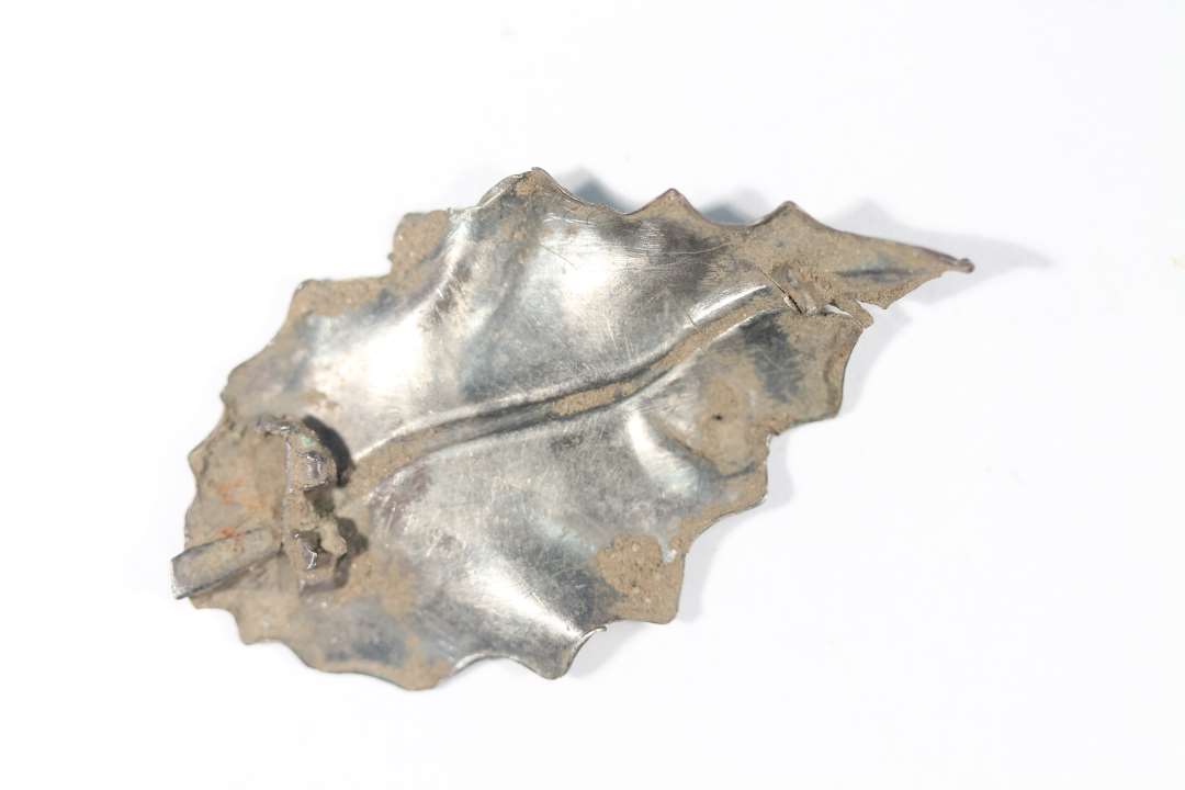 Fragment af sølvbroche. Udformet som blad. Rest af afbrudt nålefæste bagpå. Mål: 5,2x2,8 cm. 1800-eller 1900-tallet?
