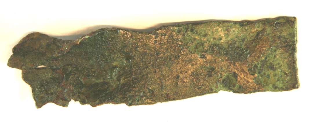 1 fragment af bronzeplade, betegnet G, af aflang form, lige overbrudt i den ene ende, forvredet og forvitret i den anden ende. L : 9,9 cm. Br : 2,6 - 7 cm. Tyk : 0,2 - 0,3 cm.