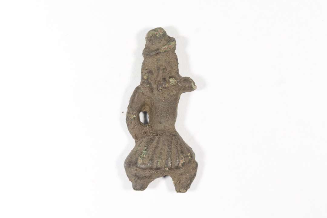 Fragment af legetøjsfigur forestillende en lille mand i 1700-tals dragt: Lang frakke, knæbukser, hat, langt hår, lang pibe. Den ane arm og underbenene mangler. Højde: 3,1 cm., bredde: 1,5 cm.
