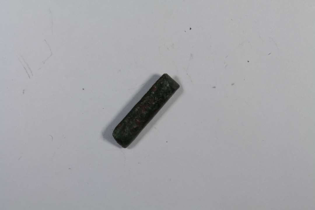Et lillebitte stangformet beslag med to nitter. Måske bæltebeslag? Længde: 1,5 cm., bredde: 0,4 cm.