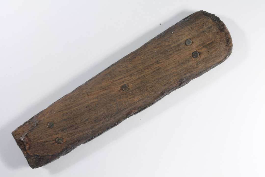 Skaft fra kniv eller andet redskab. Af to stykker træ med jern imellem. nittet sammen. Længde: 7 cm., Største bredde: 1,8 cm.