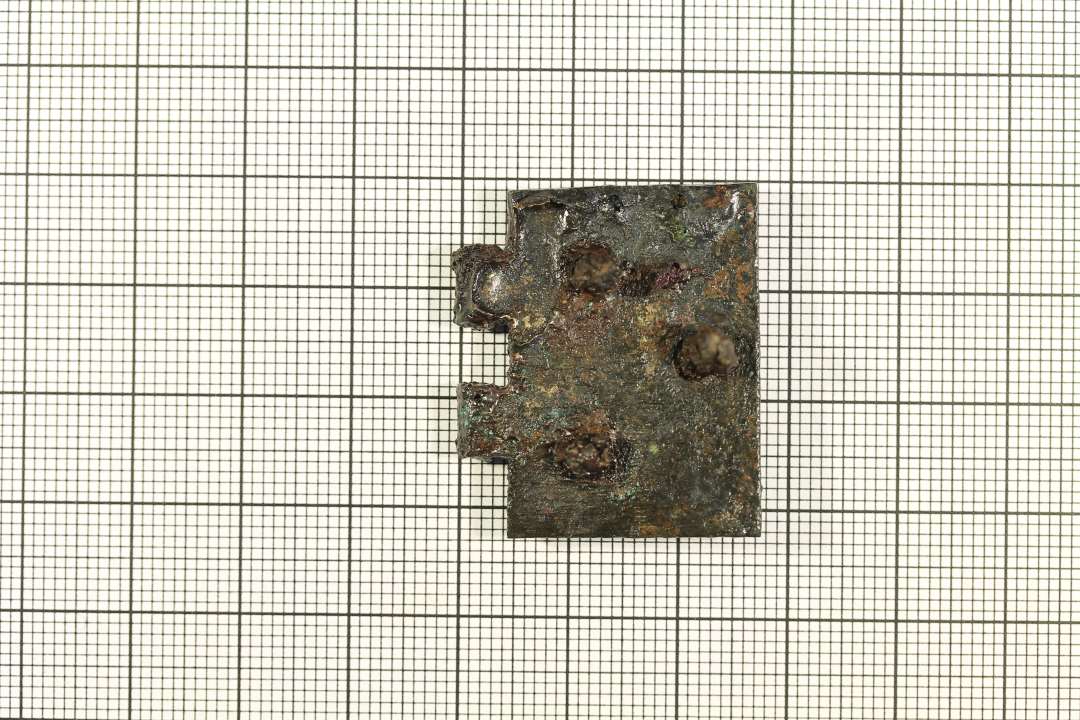 Beslag af kobberlegering. Mål: 2,2x3,2 cm., Rest af hængsel på den ene lnagside, tre isiddende nitter. Bogbeslag?

Den ene halvdel af et hængsel