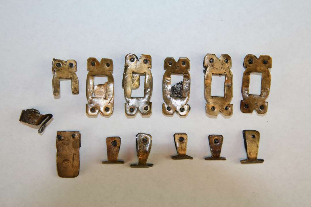 Bæltedele af bronze/kobber, seks hele og et halvt  beslag med rektangulær gennembrydning, 6 hængebeslag + div. fragmenter, samt et remendebeslag. Mål: fra 1,6-3,8 cm.

Parallel, se ASR 13x734