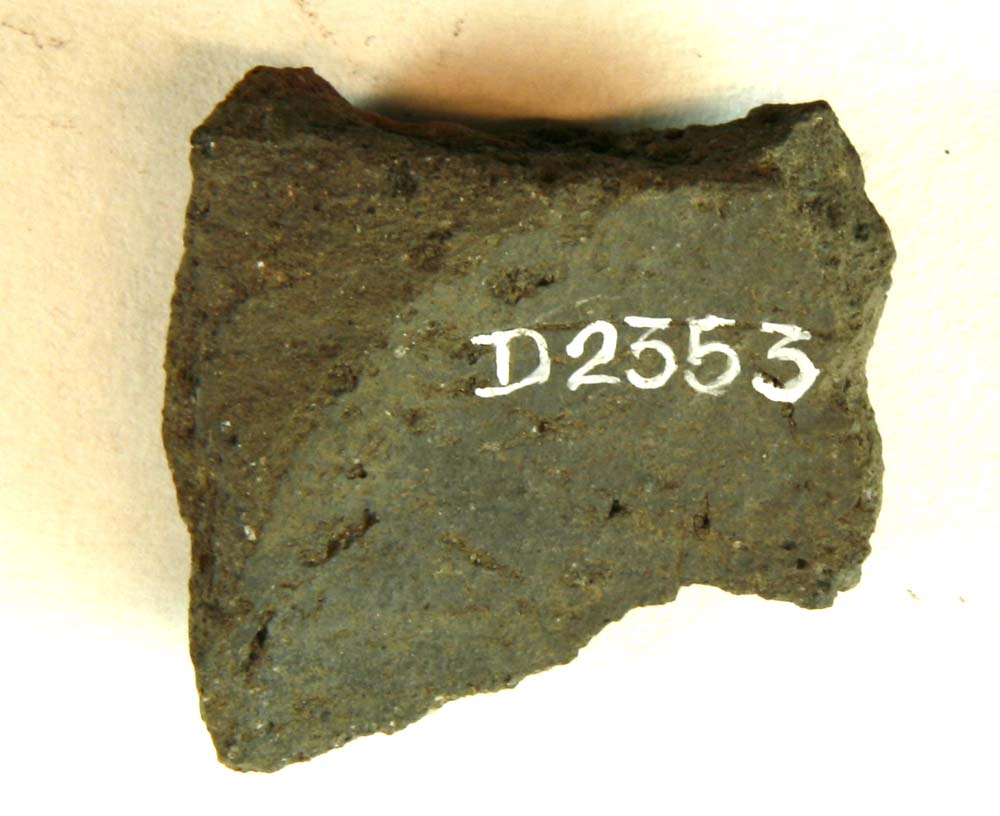 Gråsort, sintret fragment af lerklump med spor af flad cirkulær ( ? ) forsænkning.