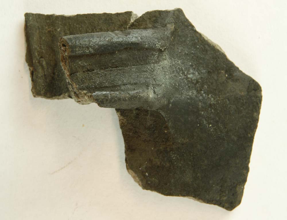Hankeskår af gråsort hårdtbrændt lergods med fragmenteret bøjlehank af oval tværsnitsform med dyb fure på oversiden. Sammenlimet med D2371.