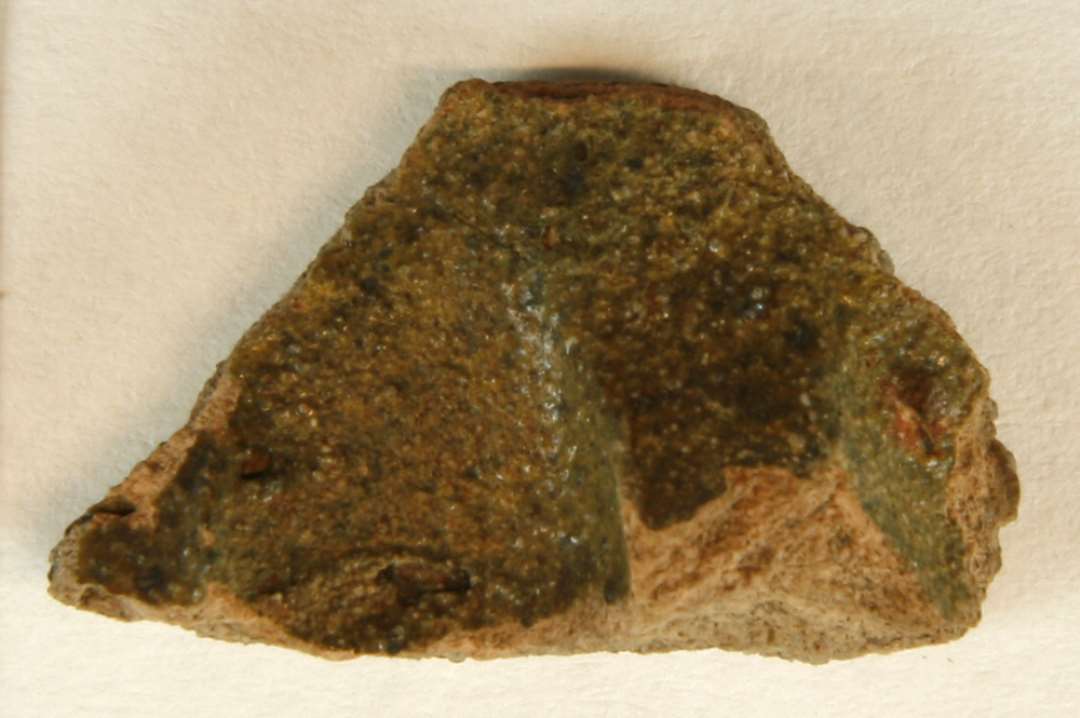 Fodrandskår af gråbrunligt lergods med indpressede fingergruber på ydersiden, der er dækket af grønlig blyglasur.