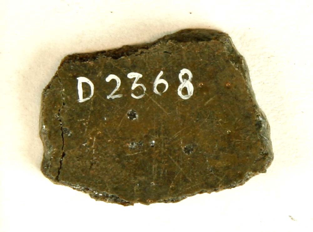 Fragment af mørk uigennemsigtig glasrude med spor af afnapning i kanten. Mål: 2,5x2 cm.Tykkelse ca. 3 mm.