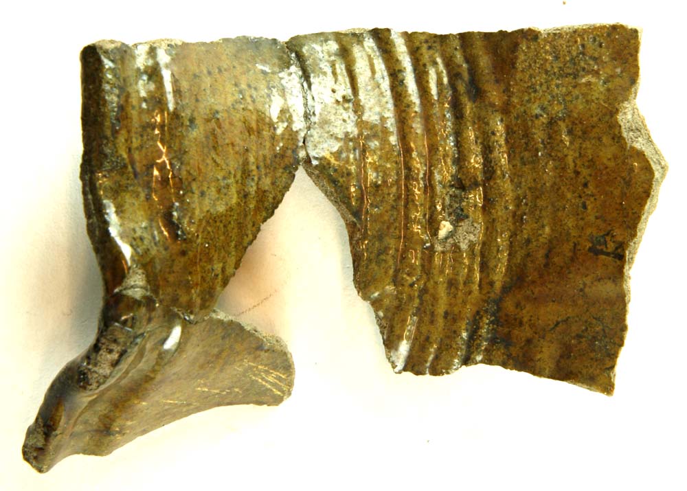 Randparti samlet af tre skår fra kande af gråbrunligt lergods med olivengrønlig blyglasur på ydersiden og delvis på indersiden. Mundingsranden er glat afrundet og udstyret med svagt fremtrædende afhældningstud. En fure og en vulst findes umiddelbart nedenfor mundingsranden, det opstående halsparti er glat, medens overgangen mellem hals og skulder er forsynet med tætte omkringløbende furer og vulster. Det stærkt udbugede skulderparti fremtræder med flade udpressede udbulinger. Sammenhørende med D2380b?