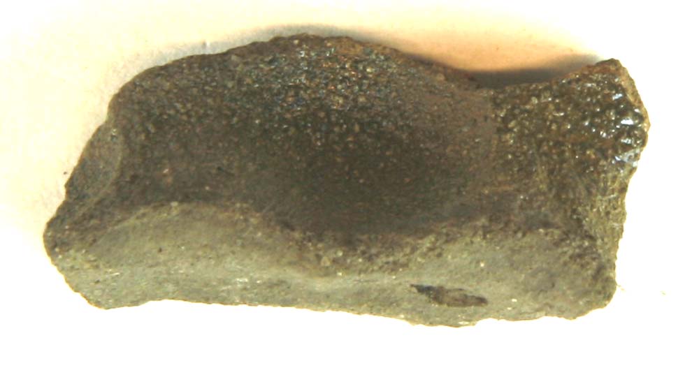 Bundskår af gråbrunligt lergods fra kande med fodrand, hvori ret svage fingergruber. Ydersiden er delvis dækket af tynd grønlig blyglasur.
