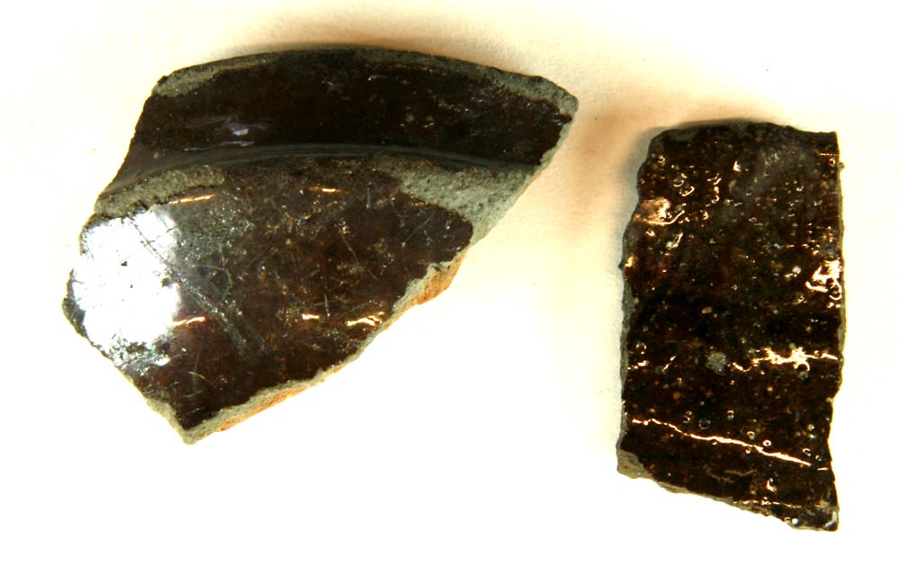 To randskår af kander af brungråt lergods med klar blyglasur på ydersiden, der på det ene skår har kraftig udbuklet omkringløbende vulst under mundingskanten, hvilken på begge er glat og afrundet.