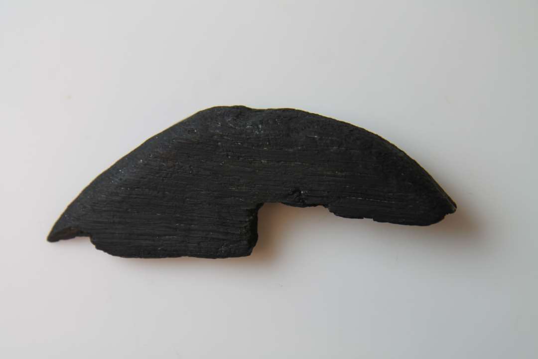 Et stykke forarbejdet træ. Måske fragment af et låg? Oprindeligt cirkulær eller halvcirkulær genstand, diameter: ca 14 cm., tykkelse: 2,4 cm.. Med rest af udskæring?
