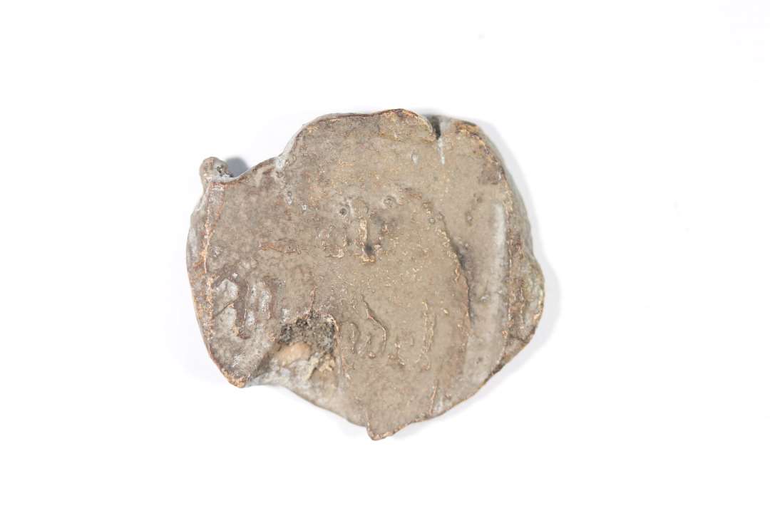 Fragment af klædeplombe af bly. Rest af præg, våbenskjold. Diameter: 3 cm.