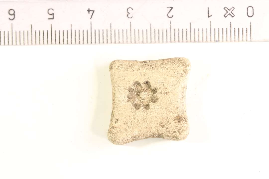 Vægtlod af bly. Pudeformet, sidelængde: 2 cm., indstemplet blomst, assymetrisk placeret, på hver side