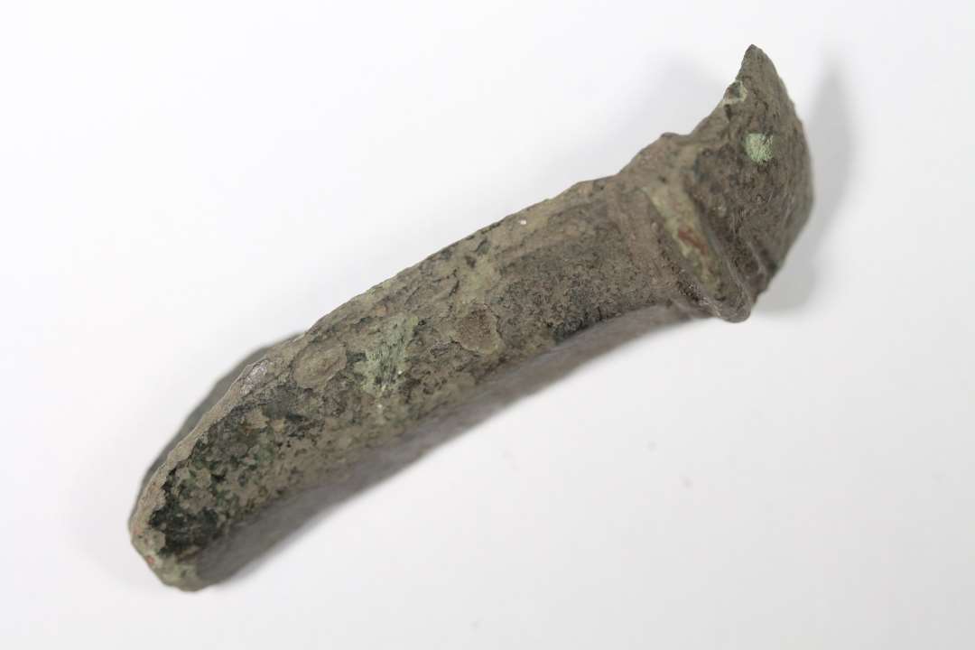Der er tale om en fod og det meste af bøjlen af en ældre romertids bronzefibula med kam på bøjlen. Længde: 4 4 cm.