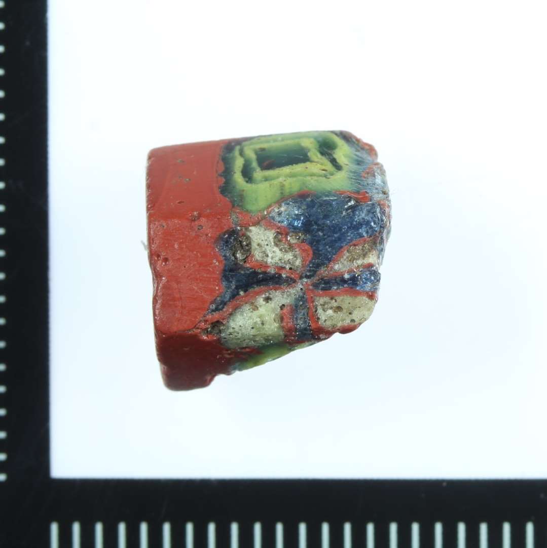 Sekskantet (sic!) med med mosaikker i form gul og blå firkant samt rød/hvid/blå 'blomst'. Grundformen i enden rødbrun. Knækket og flækket. Lokalt produceret CF 2010.