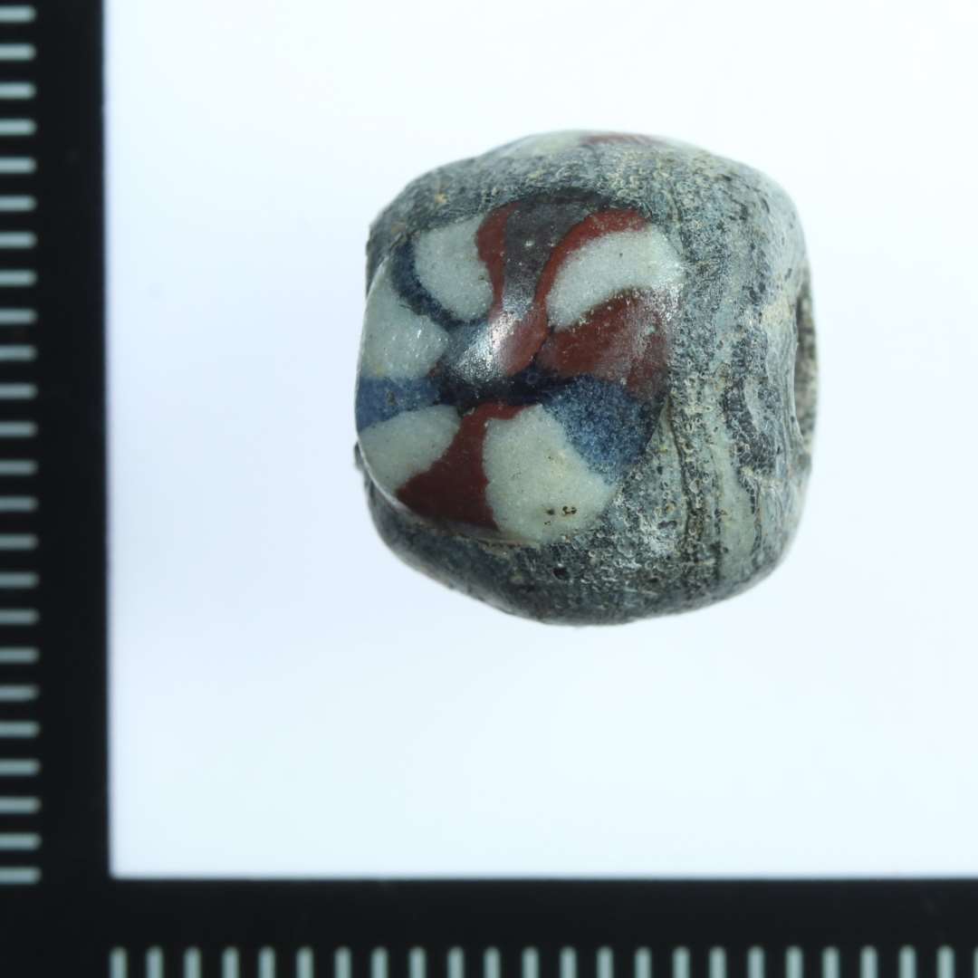 Matblå grundfarve med tre påsatte blomster eller øjer i hvid/rød/blå, sidstnævnte i glas med genskin. Kun den blå perle er mat, ikke dekorationen.