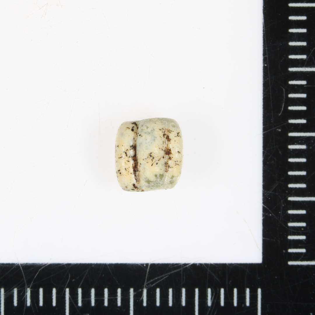 Fragment af perler med tre ribber (måske 1/5-del af perlen). Bemærkelsesværdigt lille og anløben; glaspest. Opaque, hvidlig.