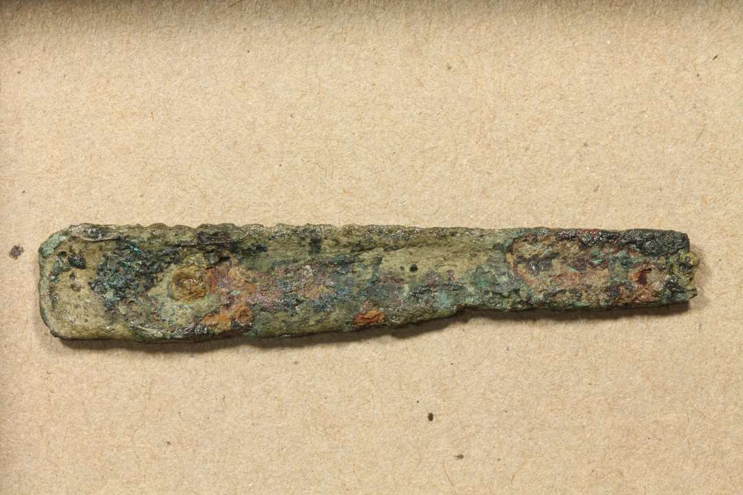Fragment af skinne 12 x 0,9 cm. Spor af to nitter. Skinnen er ornamenteret med langsgående rille. Sandsynligvis del af kam. 