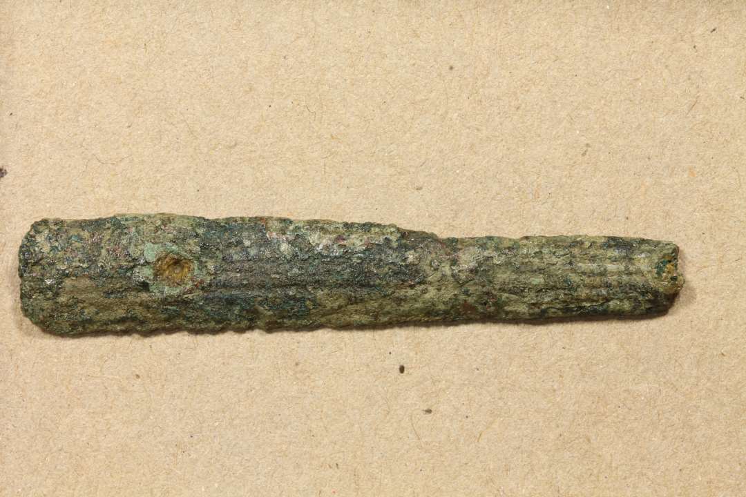 Fragment af skinne 12 x 0,9 cm. Spor af to nitter. Skinnen er ornamenteret med langsgående rille. Sandsynligvis del af kam. 