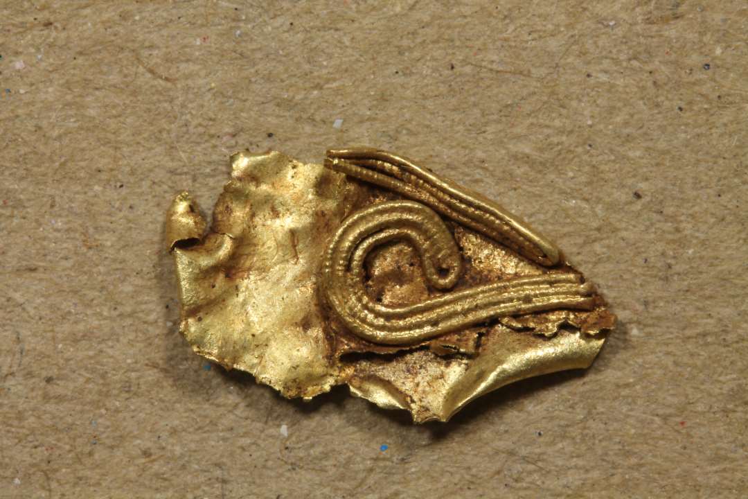 Mindre fragment (1,3 x 0,7 cm) af guldblik ornamenteret med filigran. Længde: 1,2 cm.