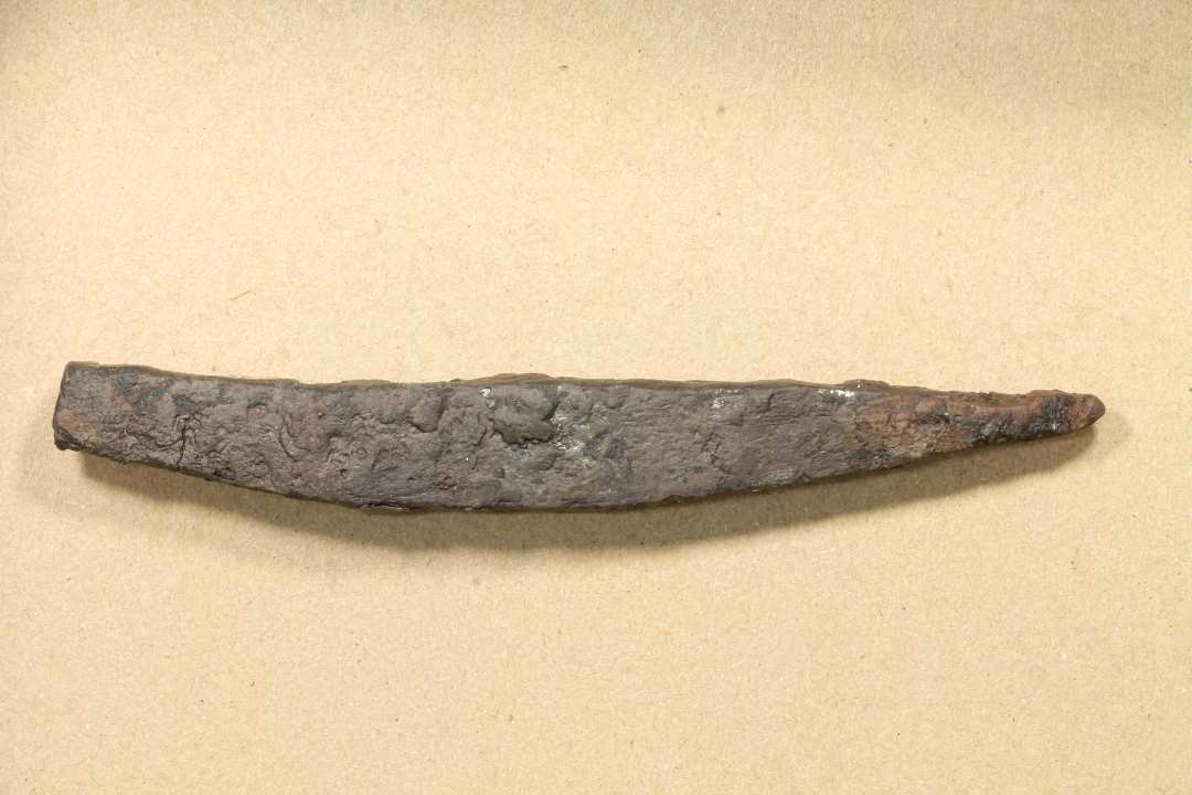 Svagt buet og tilspidset jernbarre (11,5 x 1,4 cm) med svage slagmærker i stump ende. Mulig punsel. 