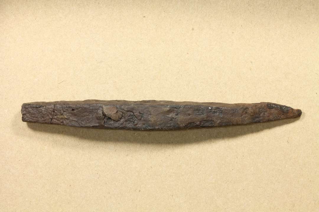 Svagt buet og tilspidset jernbarre (11,5 x 1,4 cm) med svage slagmærker i stump ende. Mulig punsel. 
