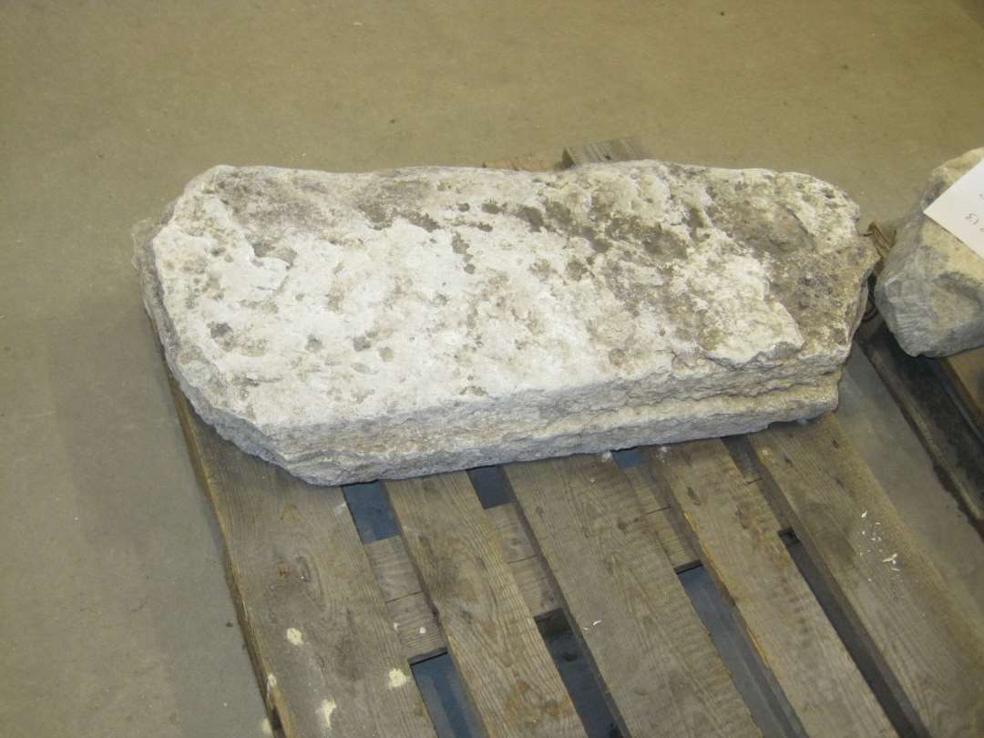 Fragment af unggotisk gravsten af kalksten. Med fals i den ene side. Mål: 100x41x12 cm.