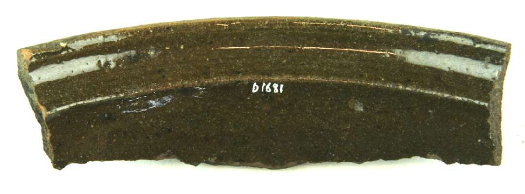 Randskår af gråbrændt lergods fra større kar (pande) med fortykket profileret mundingsrand, falset halskrave på indersiden, der er dækket af grønlig blyglasur.