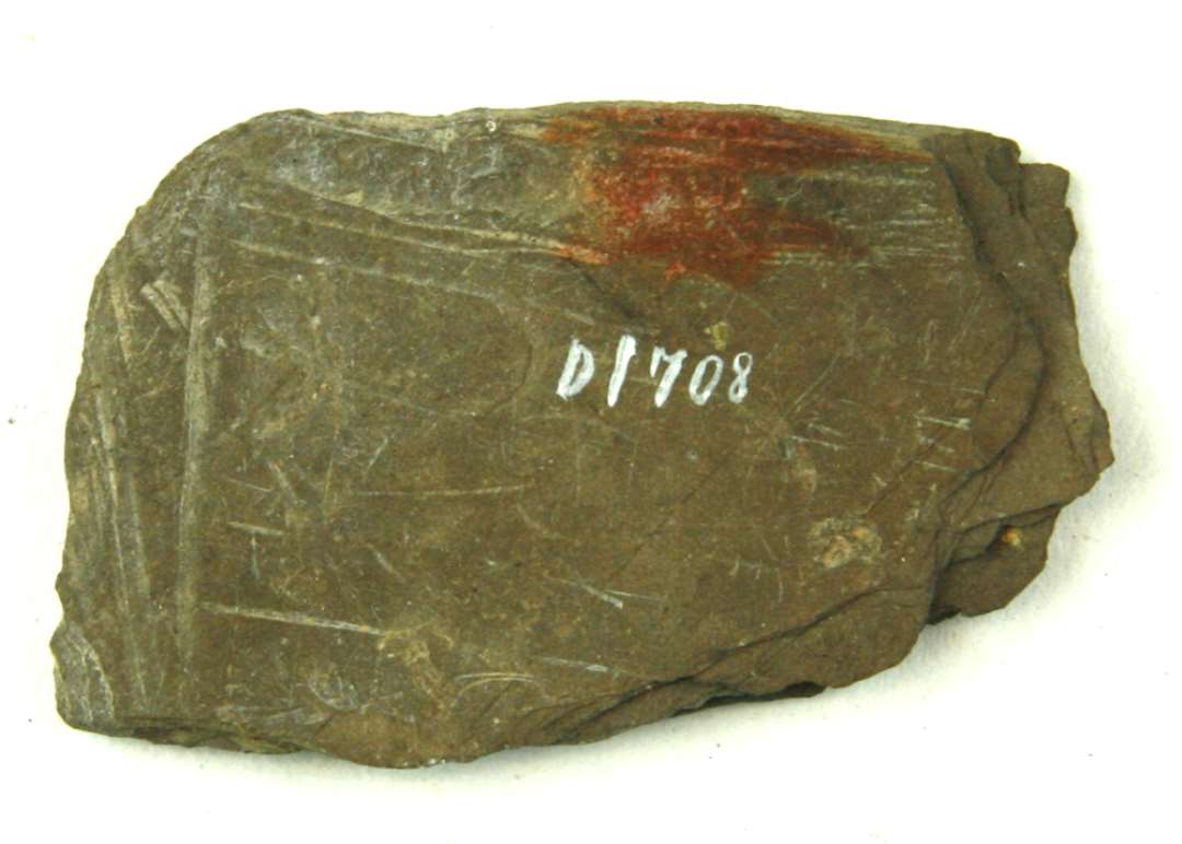 Stump af en skiferplade af rektangulær form, ca. 3,35 - 5,3 cm. Tykkelse godt 0,4 cm.
