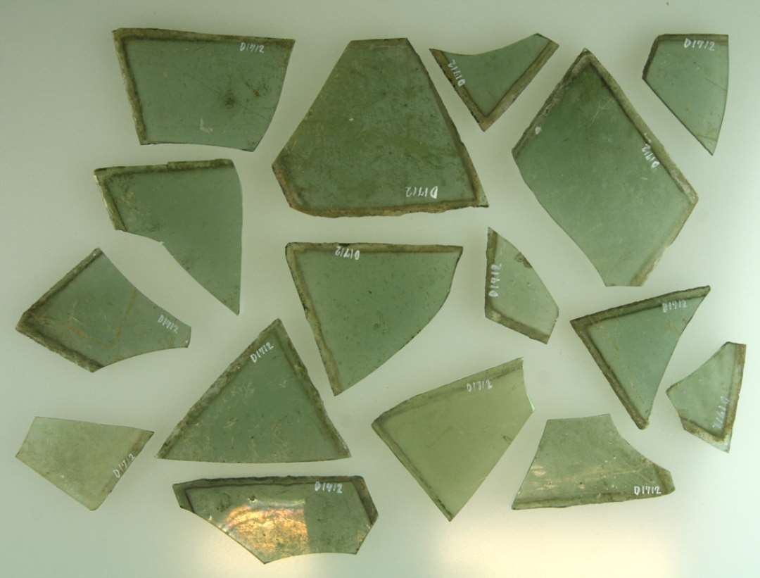 16 fragmenter af ruder af rhombeform af grønligt glas med afnappede kanter. Største mål: 3,5-8,2 cm.