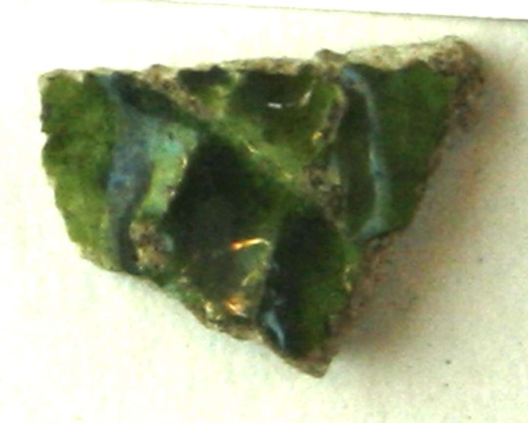 Bugskår af lysegråt, porøst pibelersaftigt gods. På ydersiden ses en stump af et pålagt bånd med indstemplede, rhombeformede fordybninger. Yder- og indersiden er dækket af grøn blyglasur.