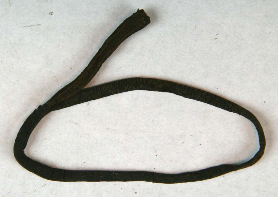 Smal læderrem, knap ½ cm. bred, 25 cm. lang, let tilstpidset i den ene ende og ca. 0,6 cm. bred i den modsatte ende.