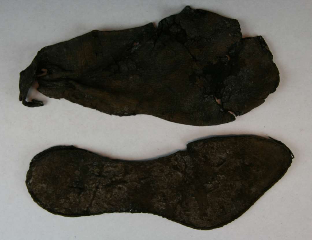1 fragmenteret sko af læder til højre fod på voksen person, af skoen er bevaret en sål med tilhørende stærkt fragmenteret overlæder. Sålen har indknebet vristparti og kraftig udsvunget fodblad i højre side samt but tilspidset tå. Sålens største længde: 25,5 cm. Største bredde over fodblad: 9 cm. over hæl: 6,8 cm. i vrist: 4,7 cm. Skoens overlæder har været samlet i skråsnit ved hjælp af en nu manglende kile i venstre vristside (inderside). Skoens udforming i vristpartier er uklar; Der findes øverst på vristen i den højre side en knap 2 cm. dyb indskæring med syhuller langs randene og ud for ankelknoen på ydersiden findes tre over hinanden anbragte gennemstukne slidser på knap 0,5 cm's bredde, hvoraf de to underste hver især er dannet ved to lodretgående indsnit, den øverste tilsyneladende kun ved et vandretgående indsnit. En rem til skoens lukning har antagelig været fæstnet i disse slidser. Den bevarede del af fodåbningens rand viser syspor efter nu tabte kantbånd.