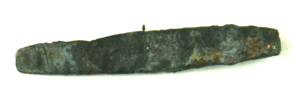 Fladt, udhamret, aflangt stump jern, bredest på midten med afsmalning mod enderne. Kanterne er jævnt afrundede. Længde: 6,5 cm. Bredde: 1,1 cm. I enderne: 0,6 cm.  Tykkelse: 0,2 - 0,25 cm.