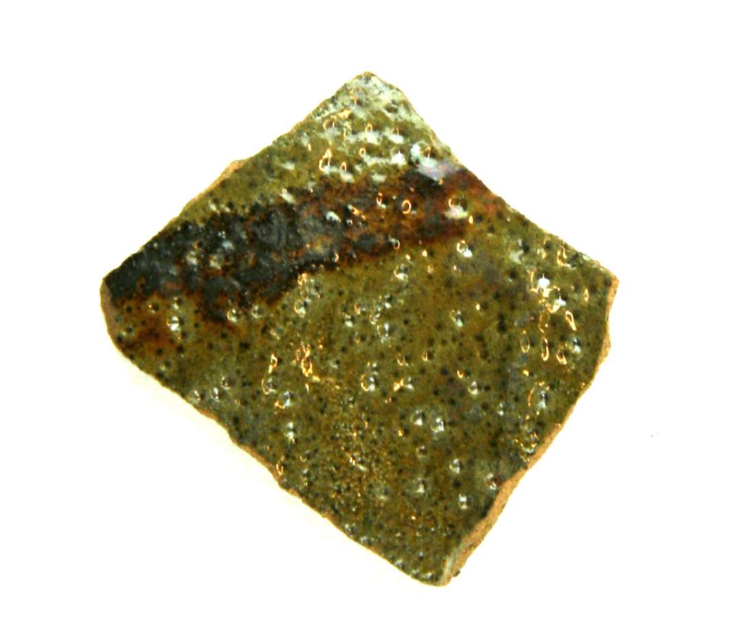Bugskår af rødbrændt lergods med gråbrændt inderside. Ydersiden er forsynet med olivengrøn blyglasur, samt en rustbrun stribe af jernoksyd. Engelsk import