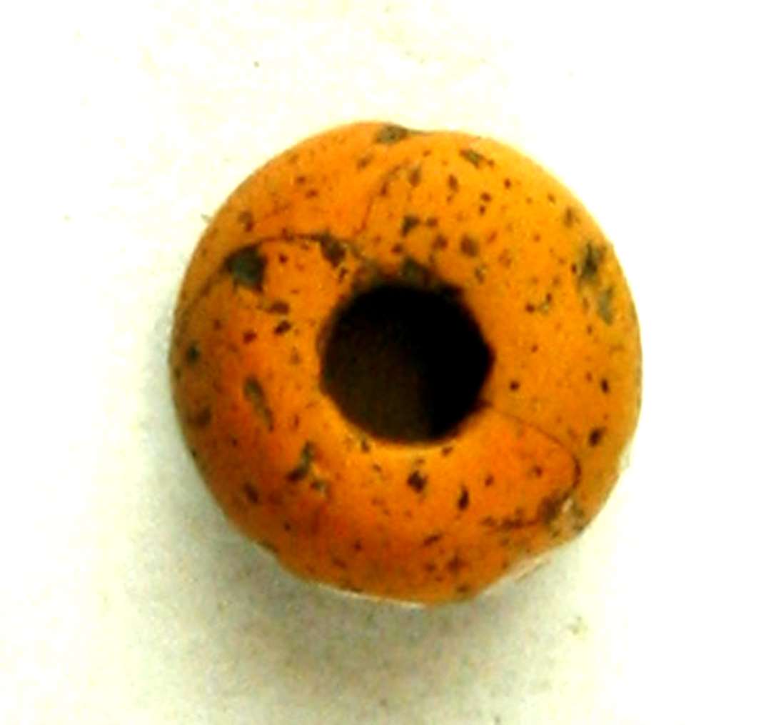 Perle af orangegullig glasmasse med talrige små gruber i overfladen. Perlen har fladtrykket tøndeform med plane endeflader og hvælvet midterparti. Snorehullet har uregelmæssig cirkulær form ca. 3 - 3,5 mm i diameter. Perlens største diameter: 0,95 - 1,0 cm. Perlens højde (tykkelse): 0,65 cm.