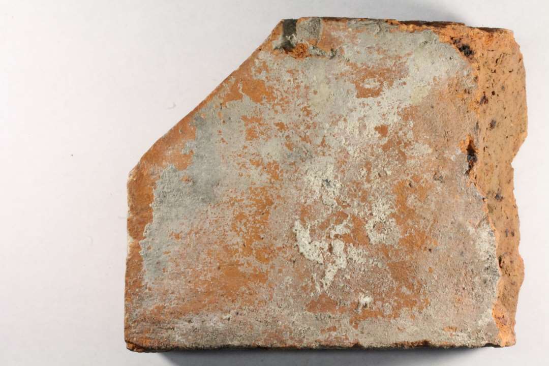 Bygningssten. Et fragment af formsten af rødbrændt ler. Stenen har form af en munkesten, hvis ene hjørne er skråt afskåret. Største bevaret længde : 16,8 cm. Bredde : 13 cm. Tykkelse : 7,2 - 7,8 cm.